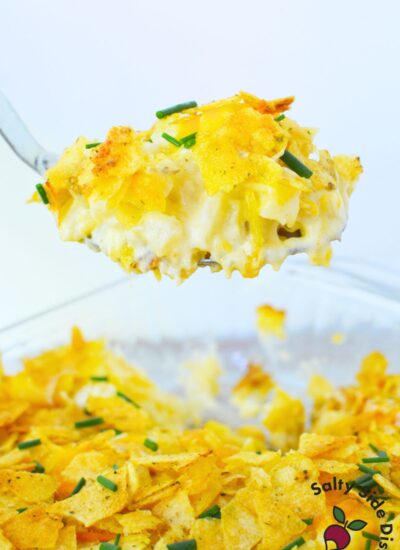 Close-up of cheesy sour cream and onion mashed potato casserole lifted from dish with golden chip topping and chives.