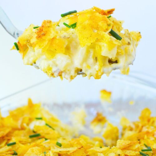 Close-up of cheesy sour cream and onion mashed potato casserole lifted from dish with golden chip topping and chives.