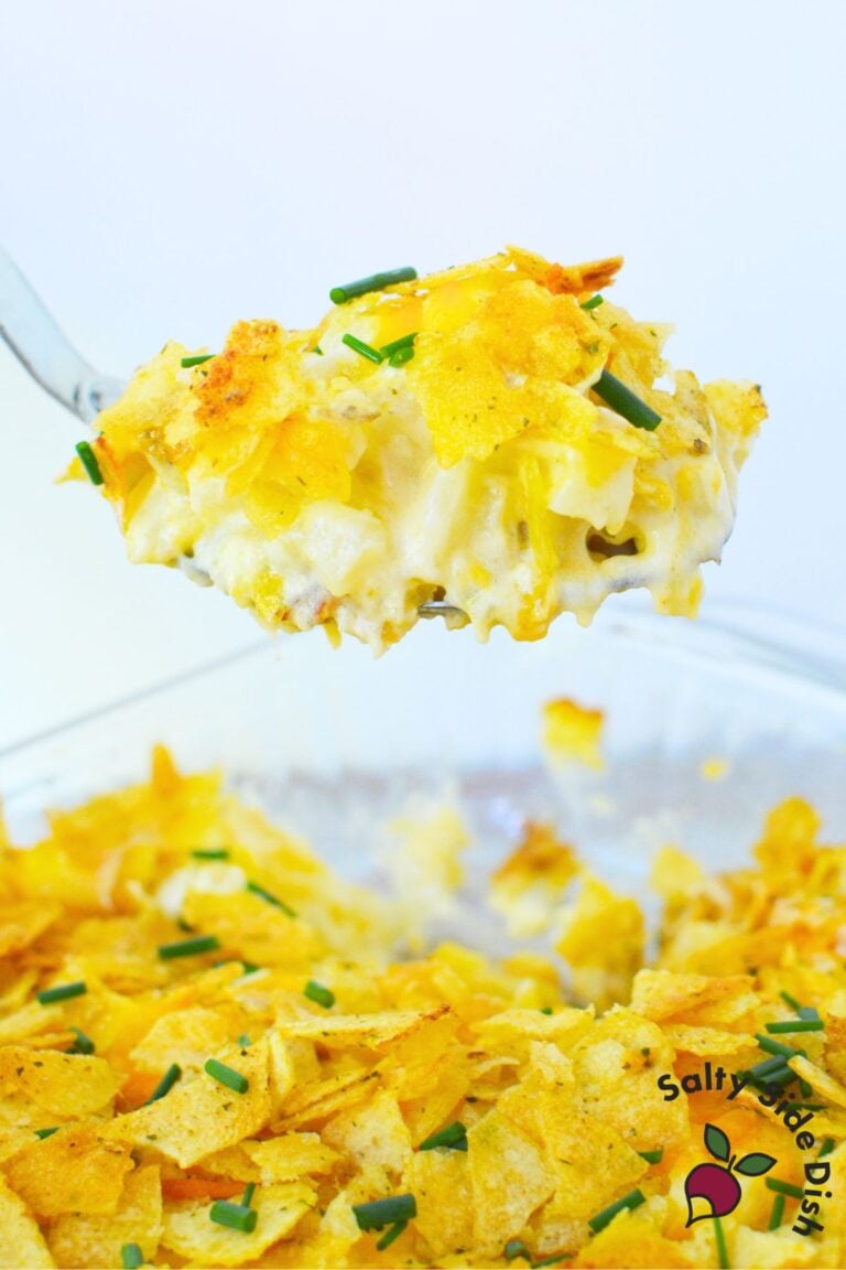 Close-up of cheesy sour cream and onion mashed potato casserole lifted from dish with golden chip topping and chives.