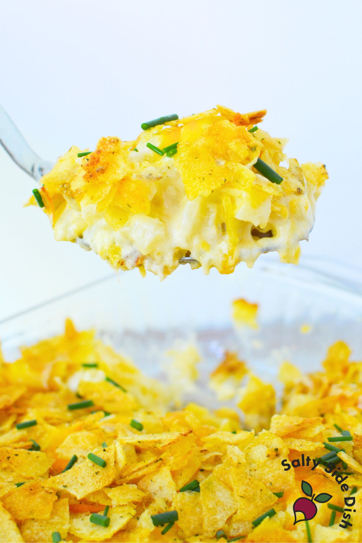 Close-up of cheesy sour cream and onion mashed potato casserole lifted from dish with golden chip topping and chives.