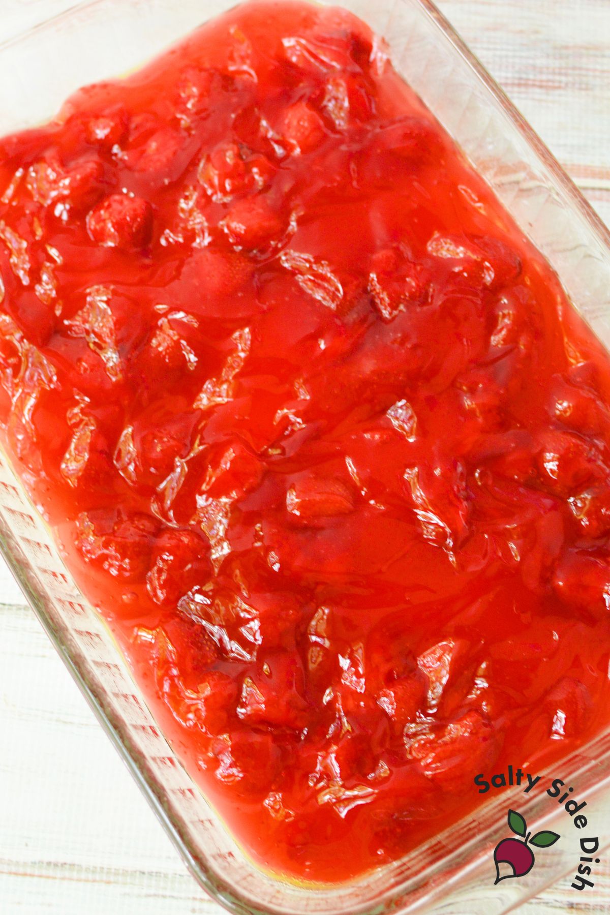 Strawberry pie filling spread in a glass baking dish for an easy strawberry dump cake recipe.
