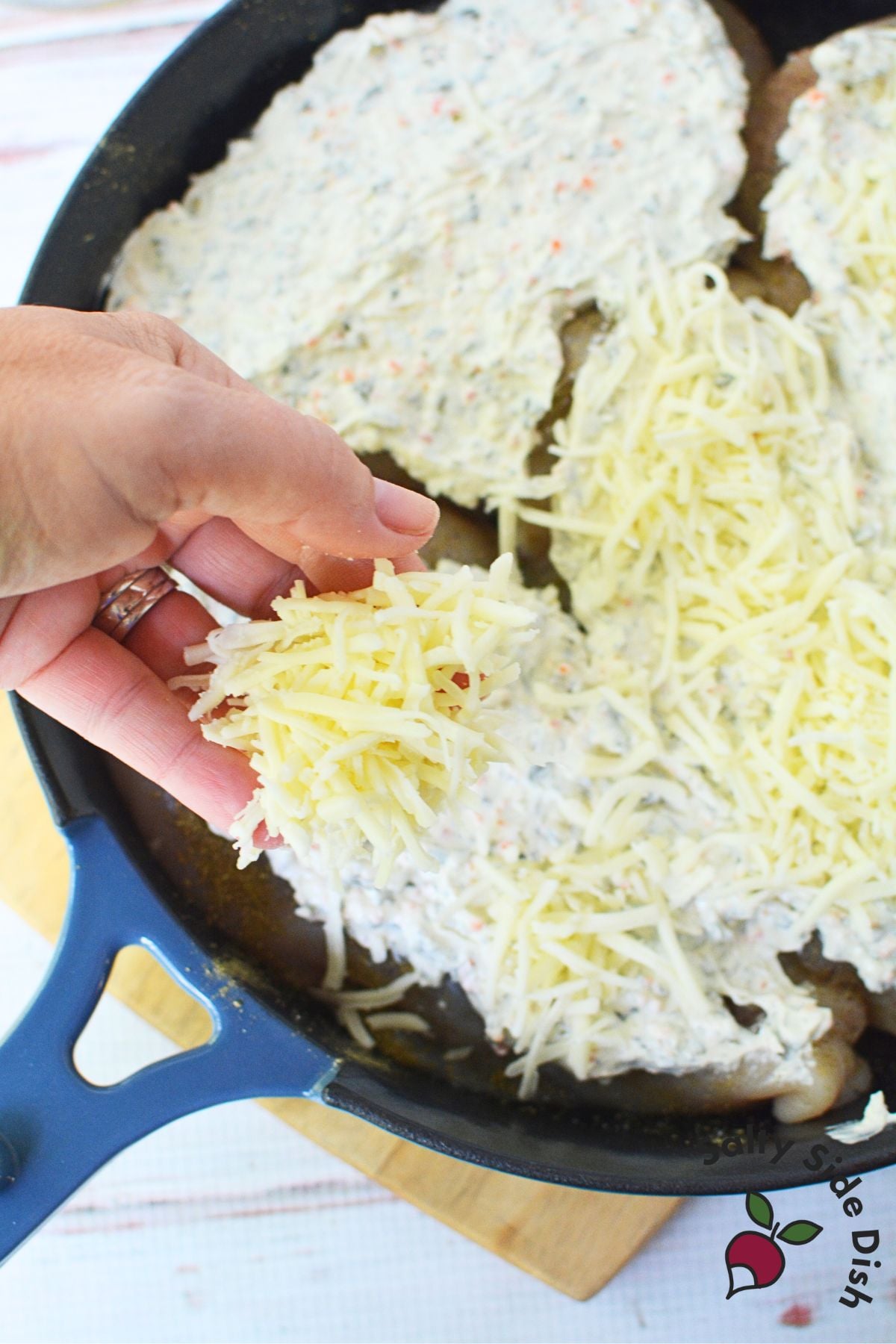 Hand adding shredded mozzarella cheese on top of chicken coated with spinach dip.