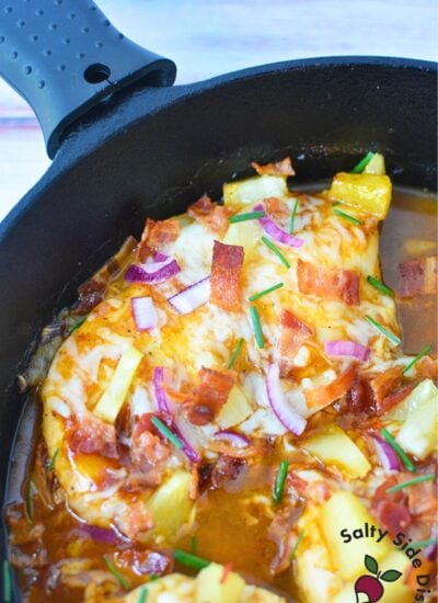 Overhead shot of unbaked Hawaiian chicken in a cast iron skillet with pineapple, bacon, red onions, and cheese.
