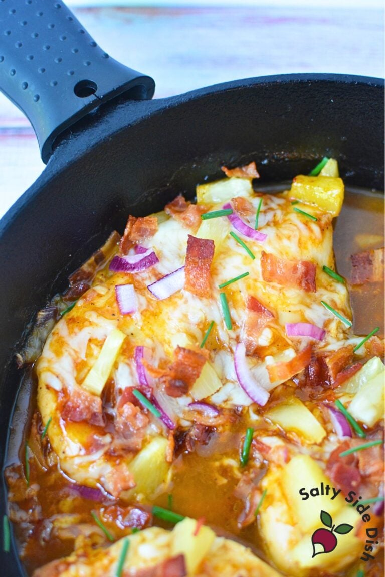 Overhead shot of unbaked Hawaiian chicken in a cast iron skillet with pineapple, bacon, red onions, and cheese.