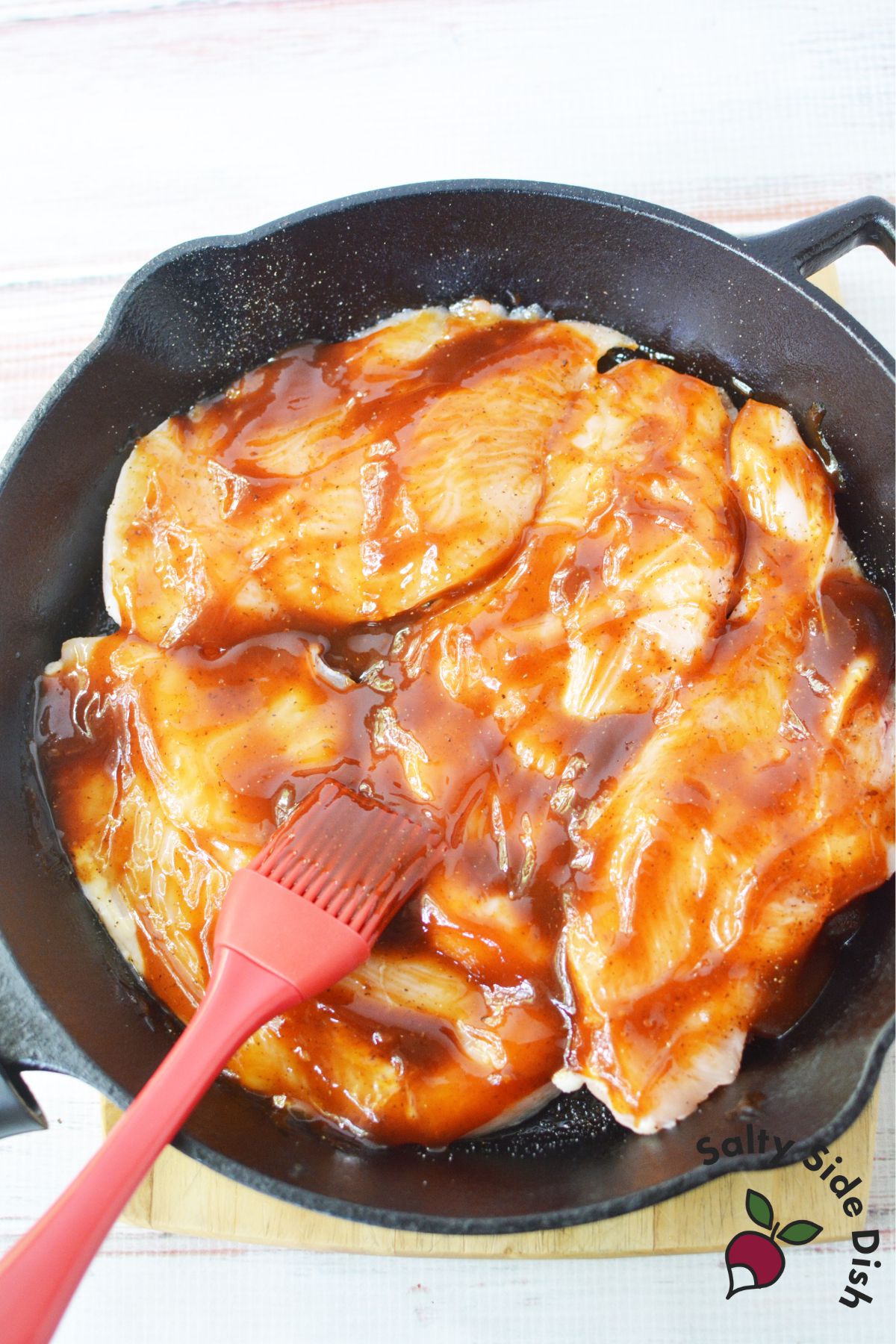 Chicken breasts brushed with barbecue sauce in a cast iron skillet.