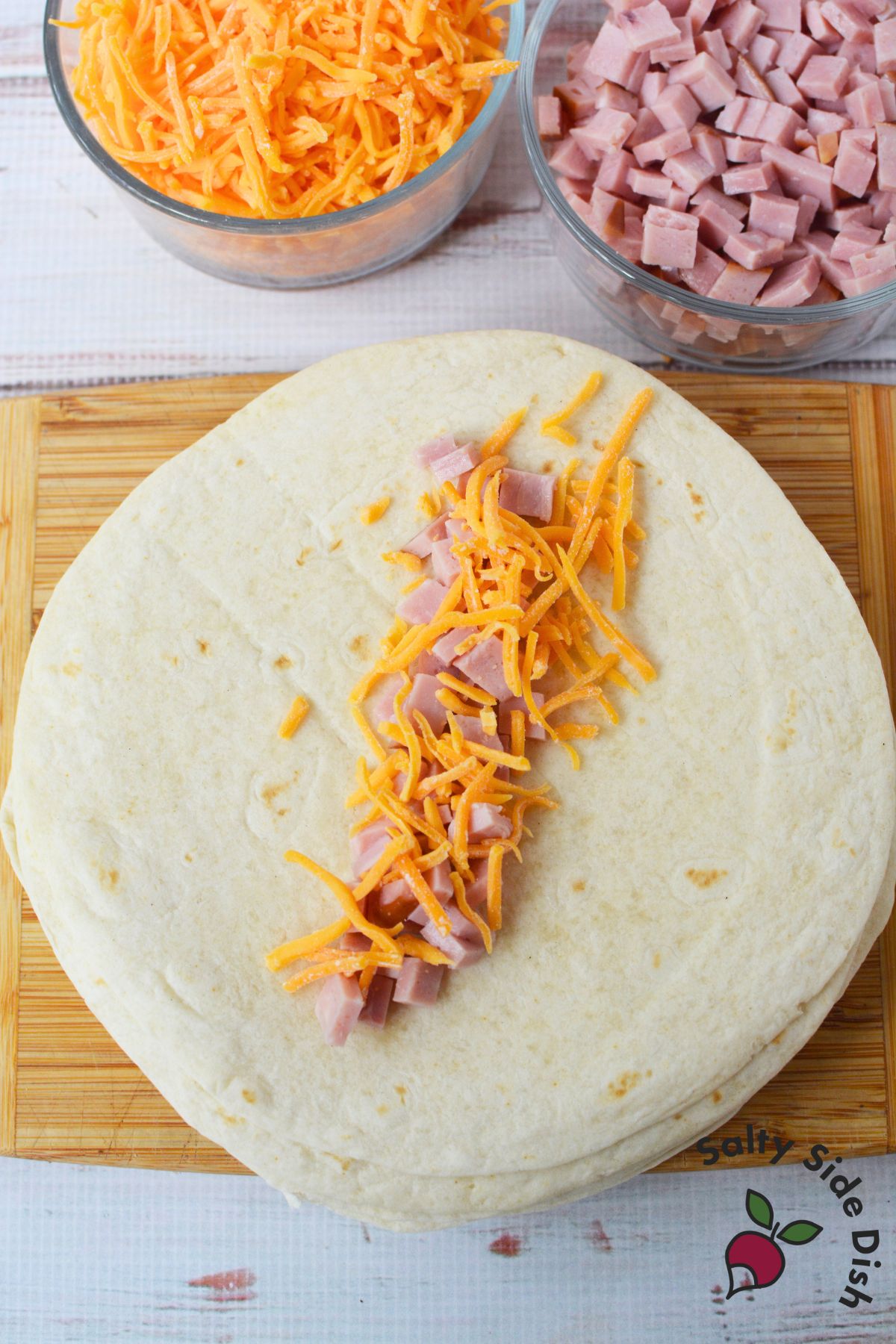 Flour tortilla filled with shredded cheddar cheese and diced ham for an easy breakfast tortilla roll-up recipe.