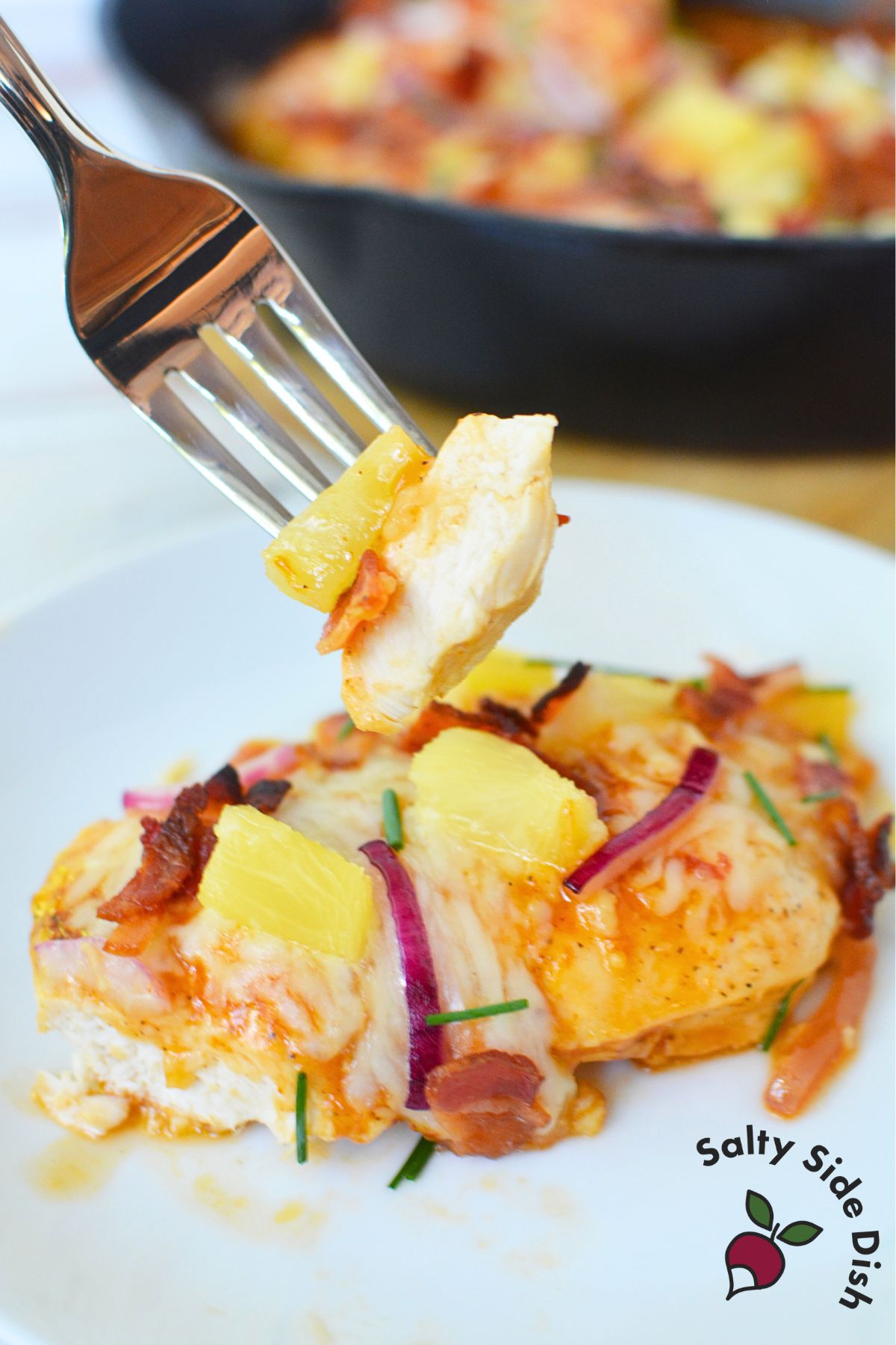 Fork holding a bite of Hawaiian chicken with pineapple, bacon, and cheese.
