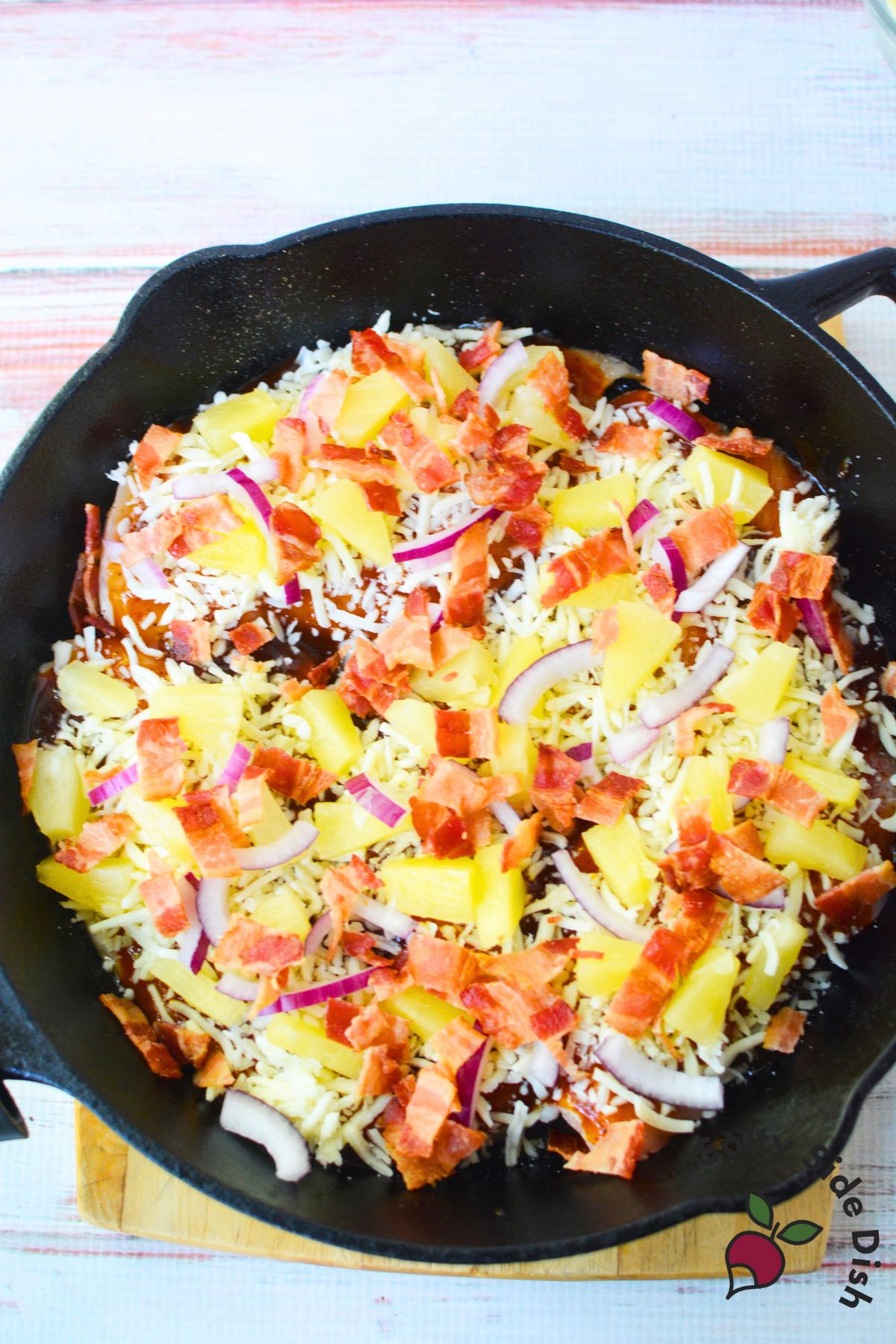 Cast iron skillet filled with baked Hawaiian chicken topped with pineapple, bacon, red onions, and cheese.