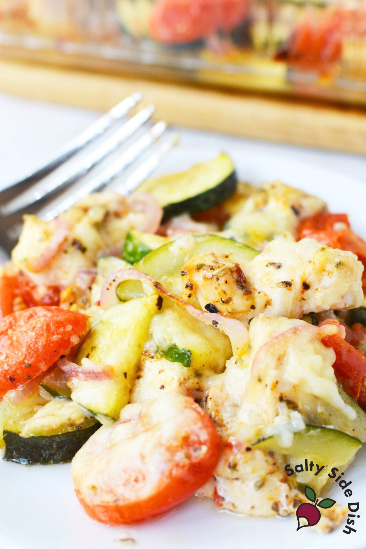Mediterranean chicken bake in a glass casserole dish with zucchini, tomatoes, and cheese.