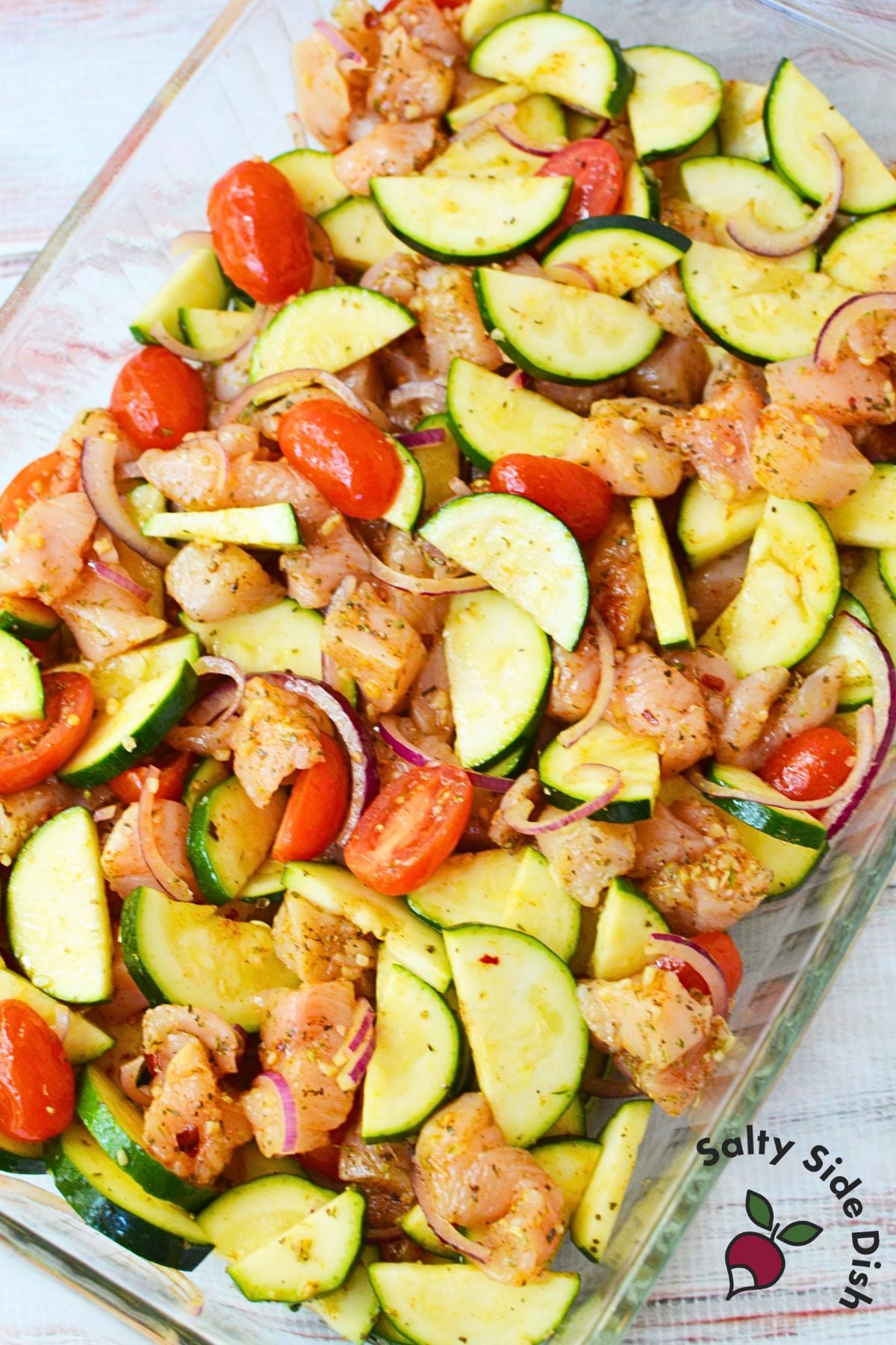 Mediterranean zucchini chicken bake ingredients arranged in a casserole dish before baking.
