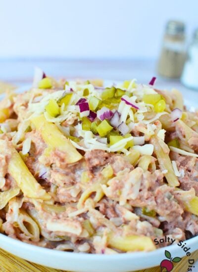 Large bowl of cold Reuben sandwich pasta salad topped with shredded Swiss, pickles, and diced red onion.