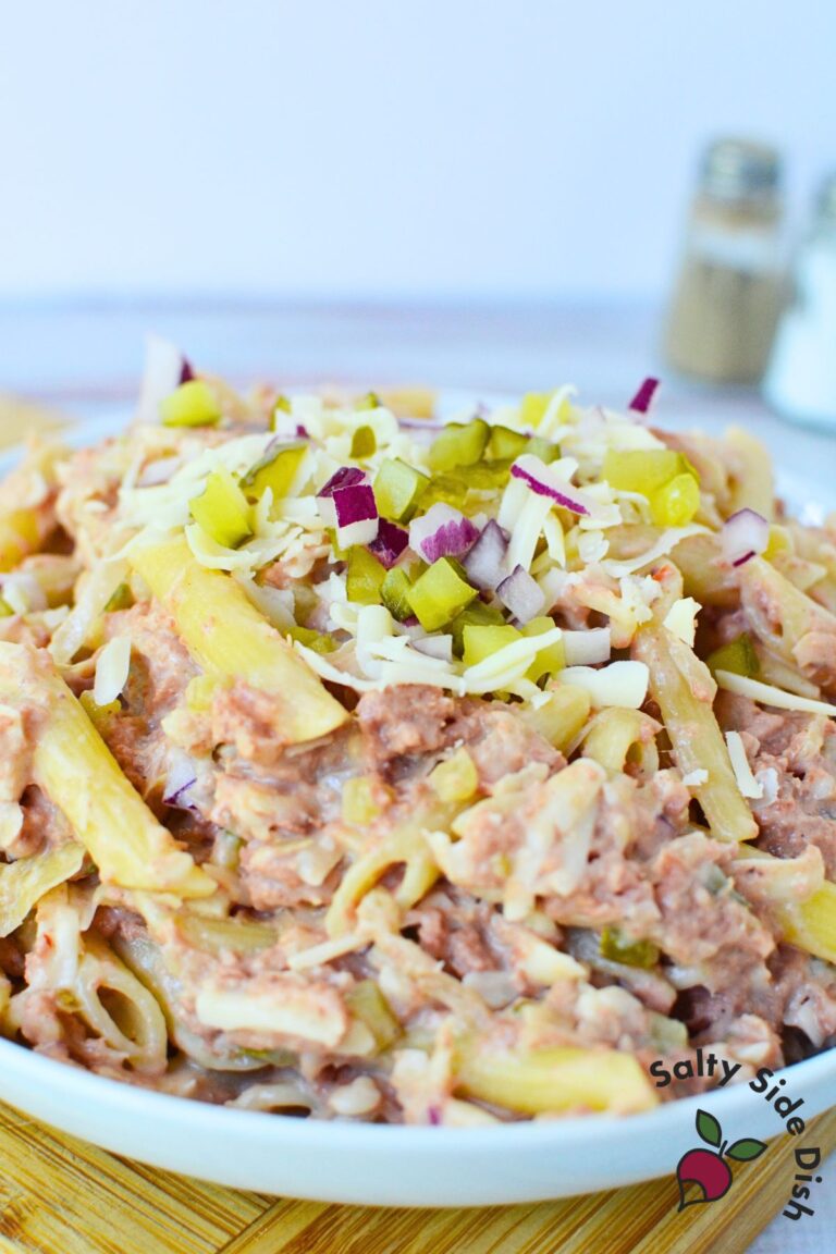 Large bowl of cold Reuben sandwich pasta salad topped with shredded Swiss, pickles, and diced red onion.