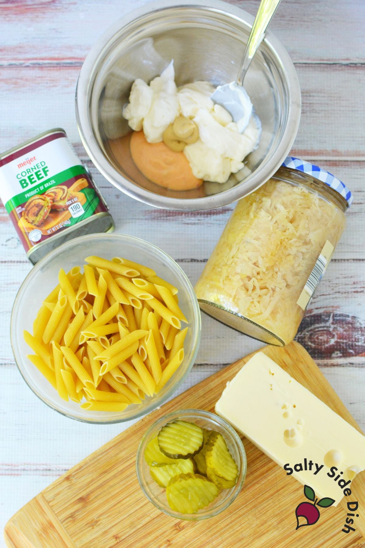 Ingredients for Reuben pasta salad with canned corned beef, penne pasta, Swiss cheese, pickles, and sauerkraut.