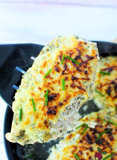 Slice of baked spinach dip chicken on a white plate with golden cheese and chives.