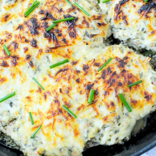 Baked spinach dip chicken in a skillet topped with melted cheese and chives.