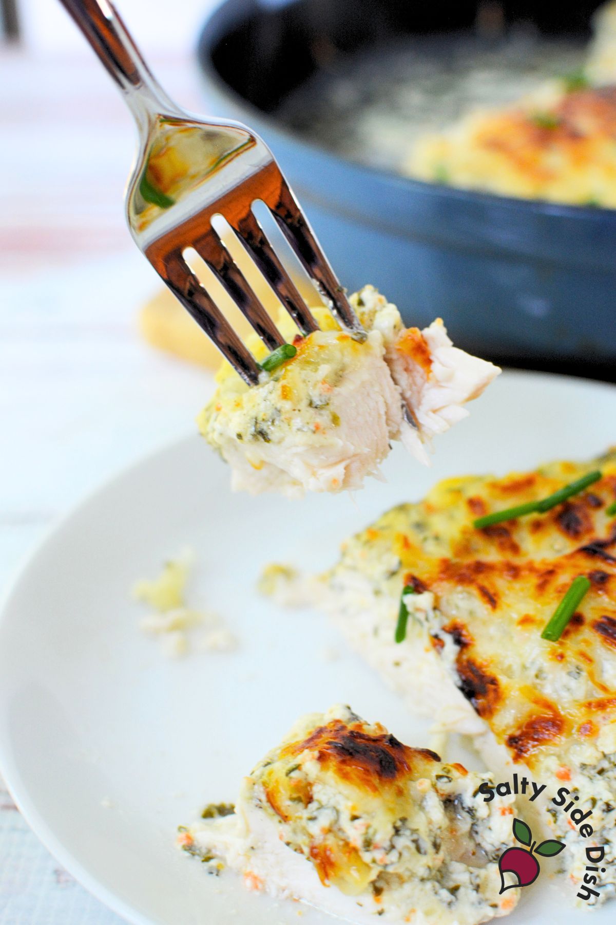 Fork holding a bite of cheesy spinach dip chicken over a plate.