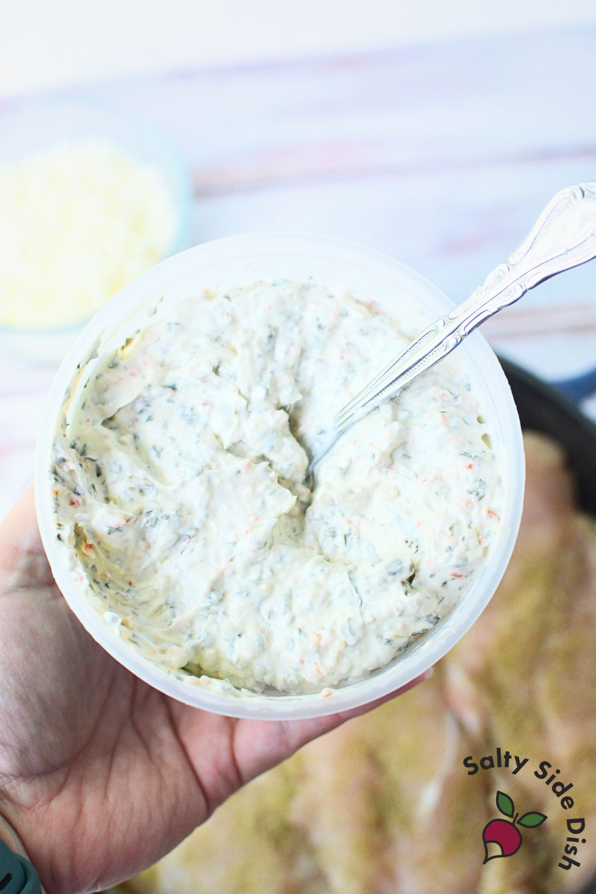 Tub of creamy spinach dip being used to make spinach dip chicken.