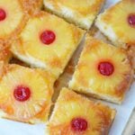 Easy pineapple upside down cake baked in a 9x13 pan, cut into squares with pineapple rings and cherries on top.