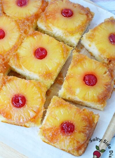 Easy pineapple upside down cake baked in a 9x13 pan, cut into squares with pineapple rings and cherries on top.