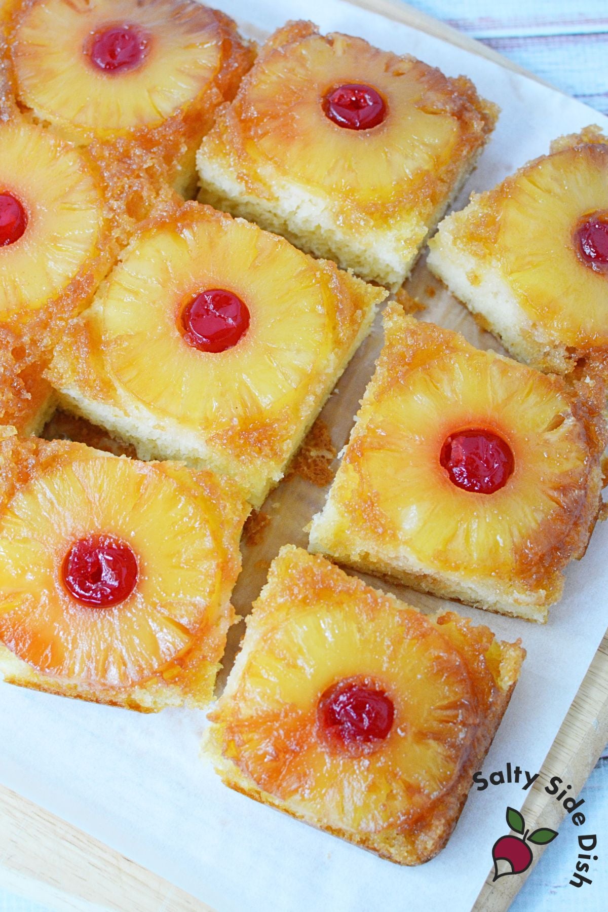 Easy pineapple upside down cake baked in a 9x13 pan, cut into squares with pineapple rings and cherries on top.