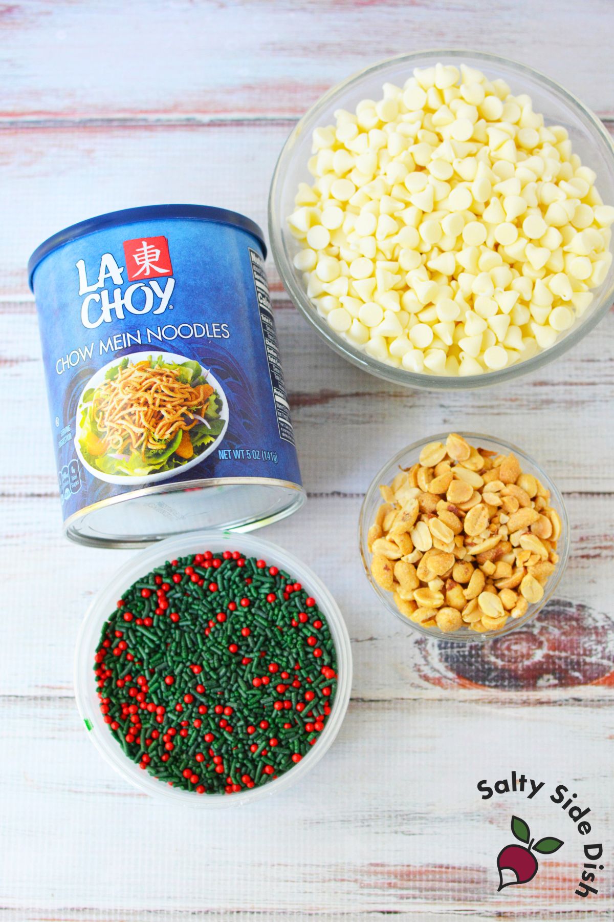 Ingredients for white chocolate haystacks including chow mein noodles, peanuts, white chocolate chips, and Christmas sprinkles