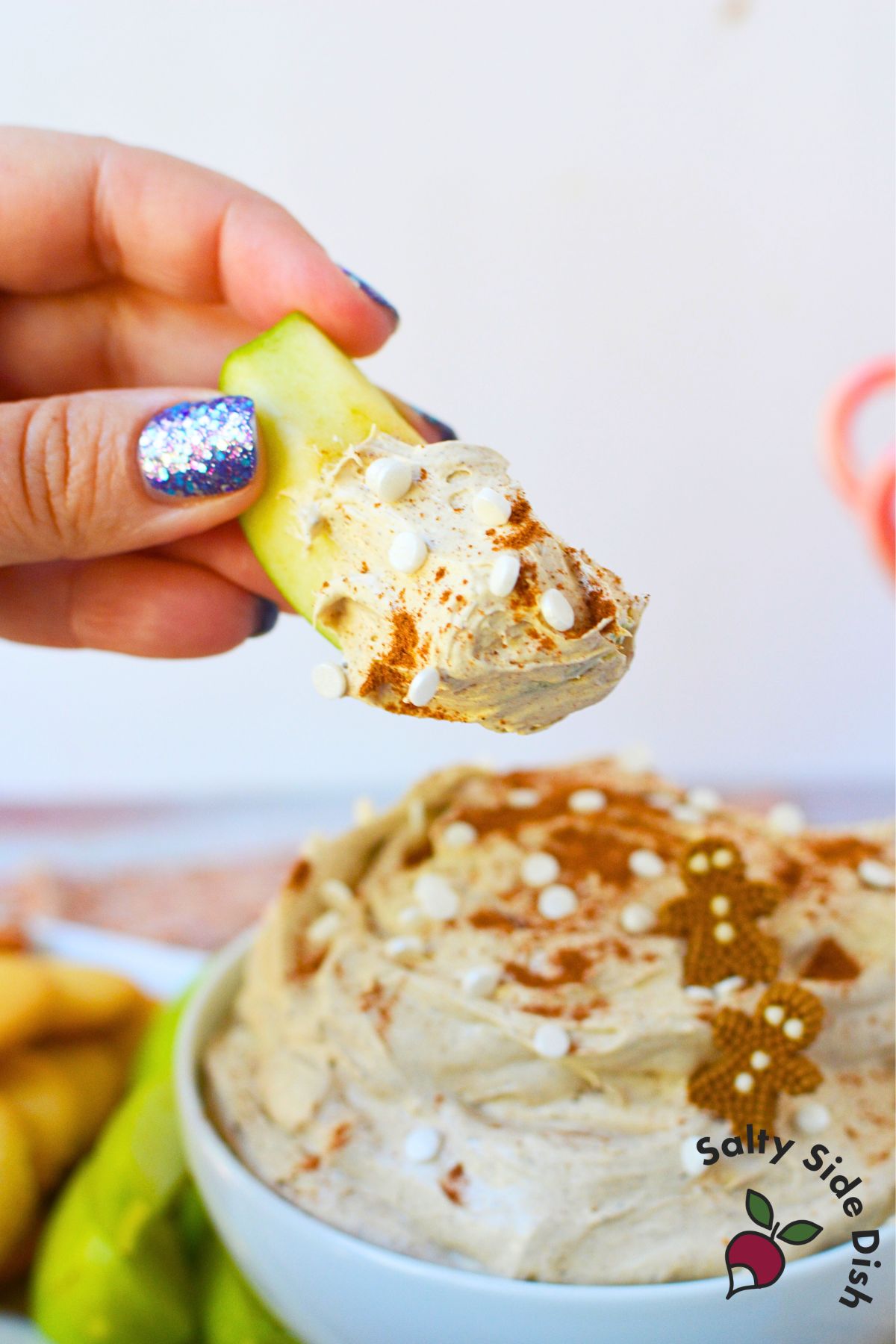 Green apple slice dipped into creamy gingerbread dip topped with cinnamon and white sprinkles.