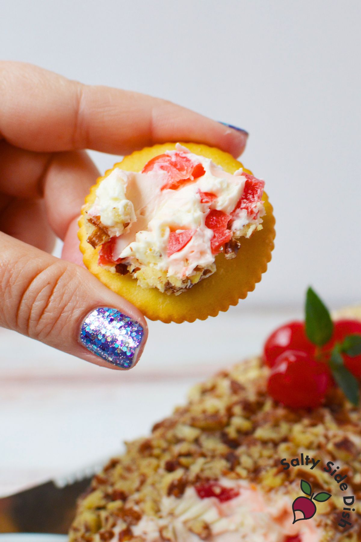 Bite of cherry cream cheese log on a cracker with maraschino cherry pieces and pecans