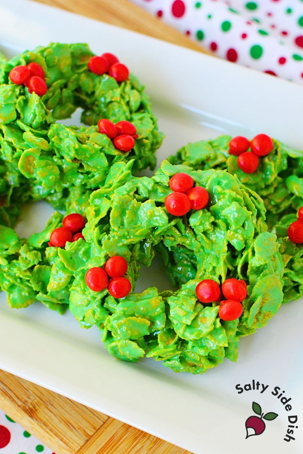 Holiday cornflake wreath cookies stacked on a platter, decorated with red candies.