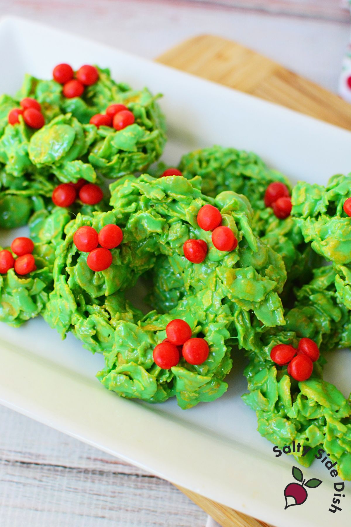 Festive cornflake Christmas wreath cookies on a white plate, decorated with red candies.