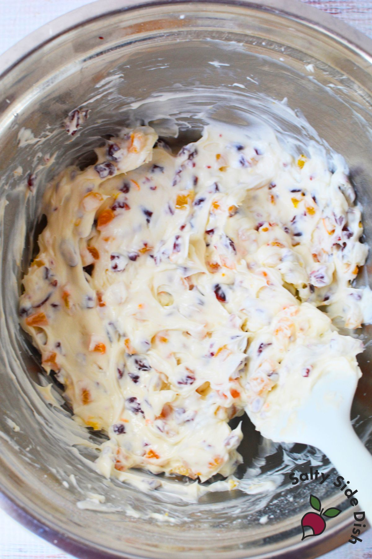 Cranberry orange cream cheese dip with dried cranberries and apricots being mixed in a stainless steel bowl”