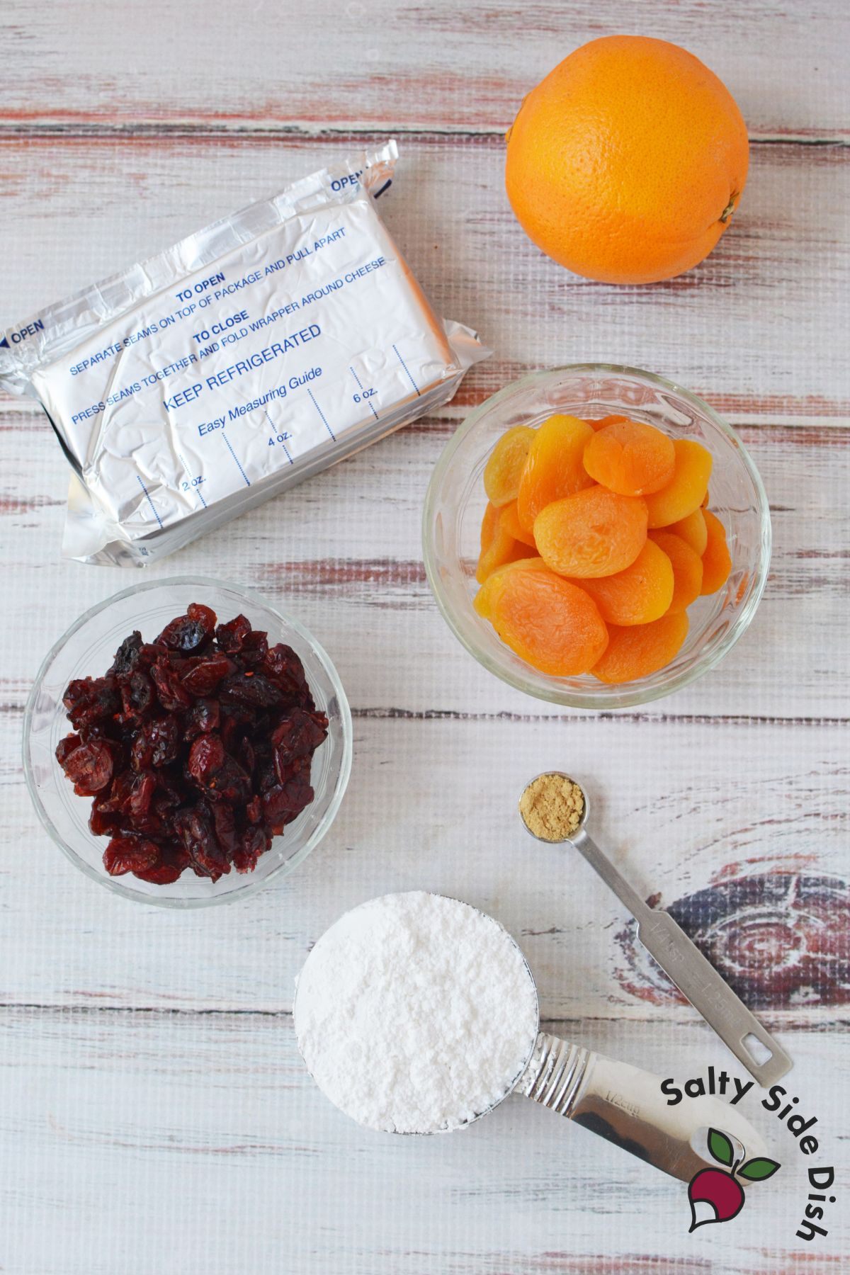 Ingredients for cranberry orange cream cheese spread including cream cheese, dried cranberries, apricots, orange, powdered sugar, and ground ginger