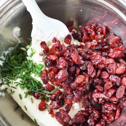 Mixing bowl with cream cheese, dried cranberries, and chopped chives for cranberry pinwheels.