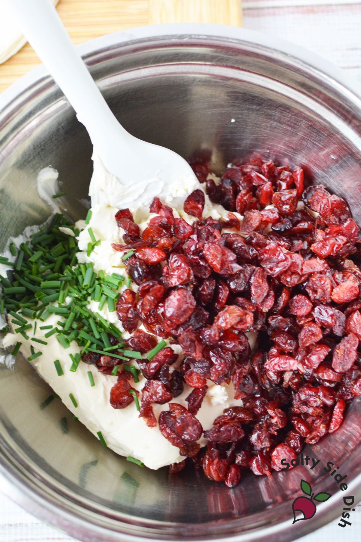 Mixing bowl with cream cheese, dried cranberries, and chopped chives for cranberry pinwheels.