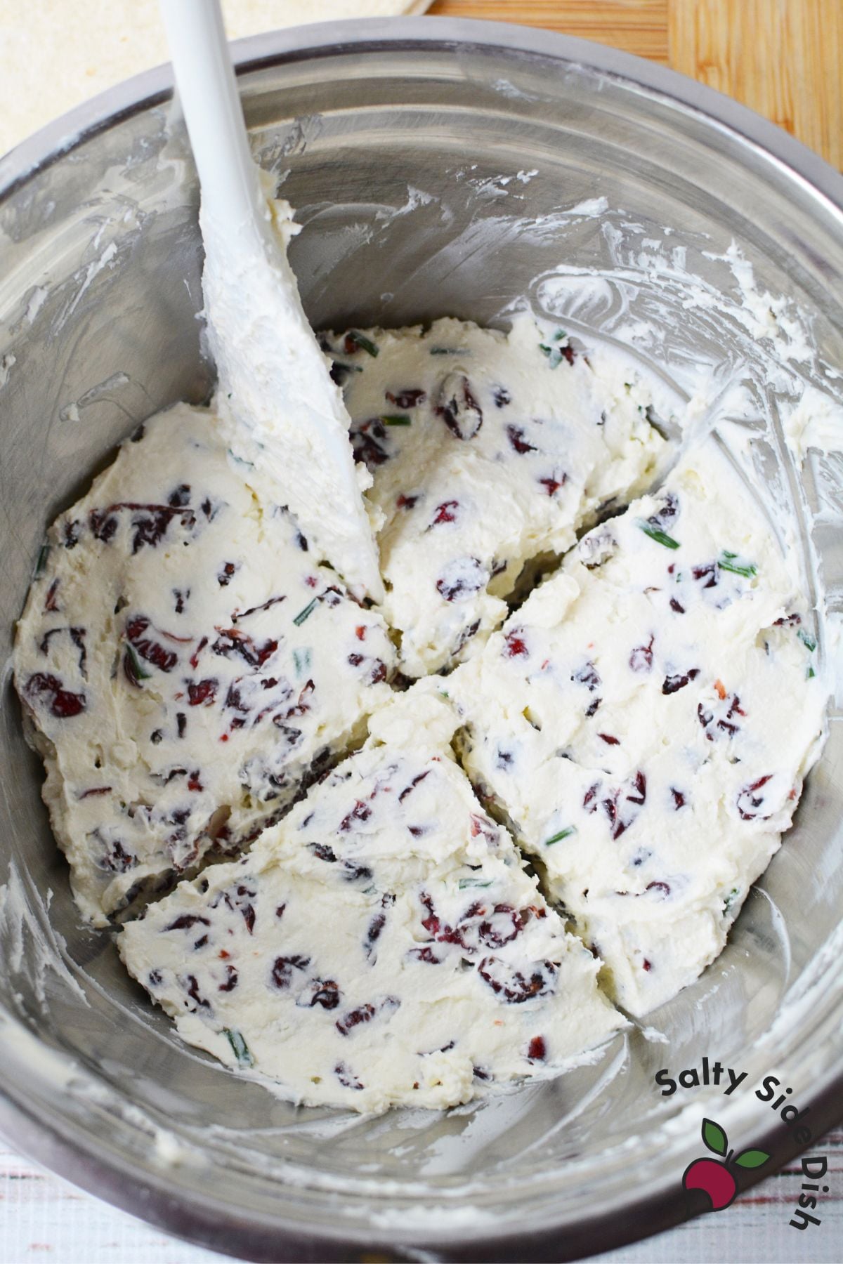 Bowl of cranberry pinwheel filling made with cream cheese, feta, dried cranberries, and chives divided into four portions.
