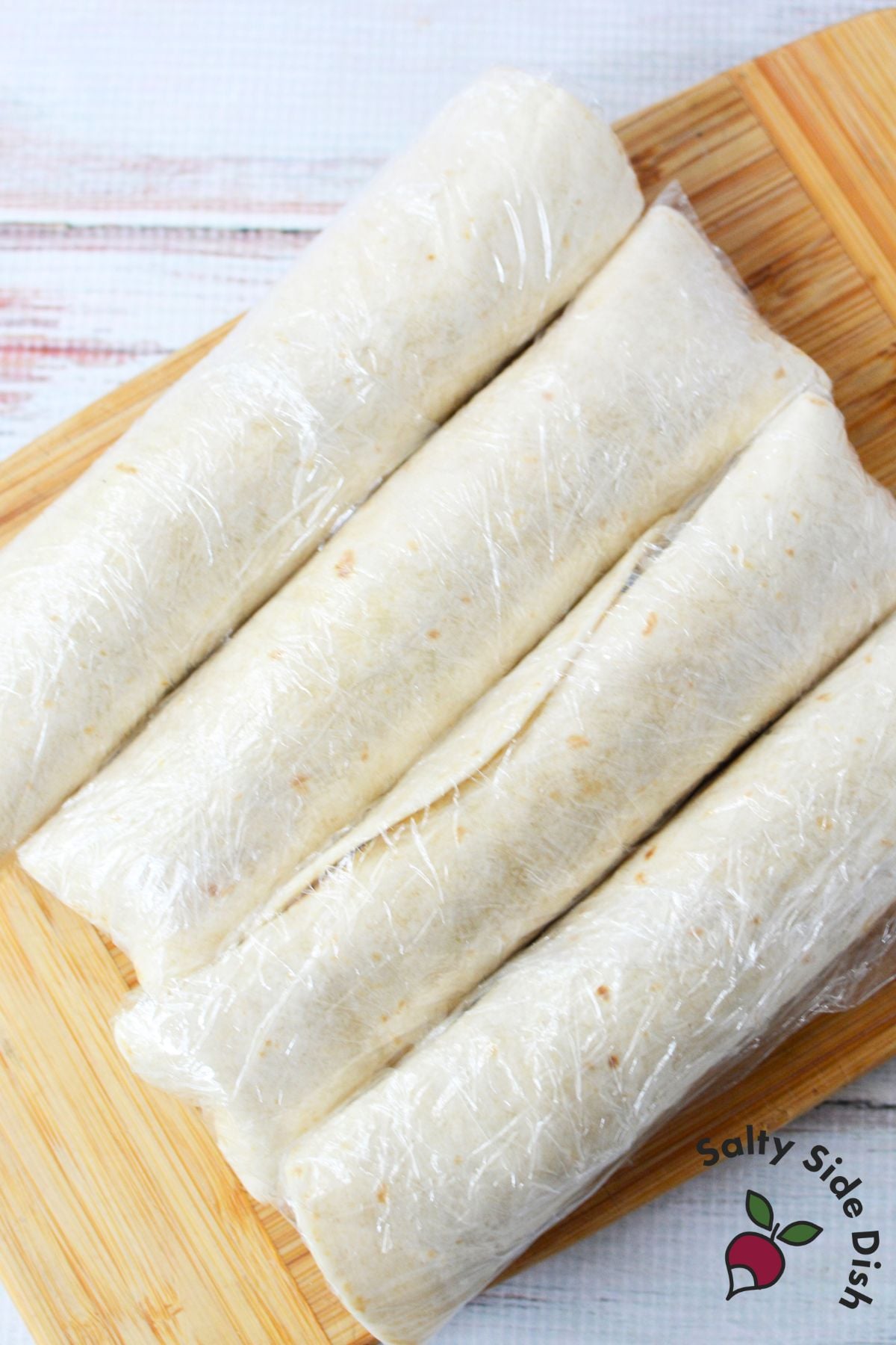 Cranberry pinwheel tortillas wrapped in plastic wrap and ready to chill in the refrigerator.