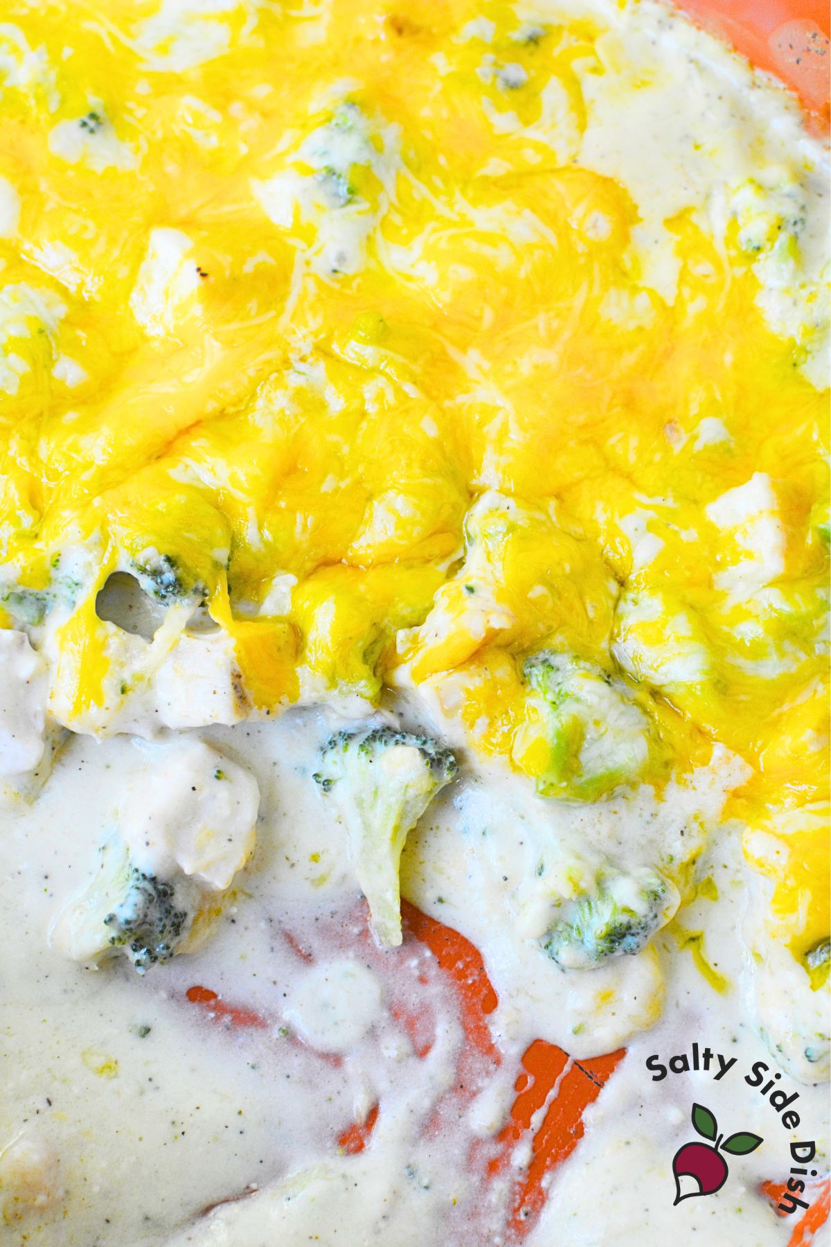 Creamy chicken broccoli casserole with bubbling sauce and melted golden cheese in orange baking dish.
