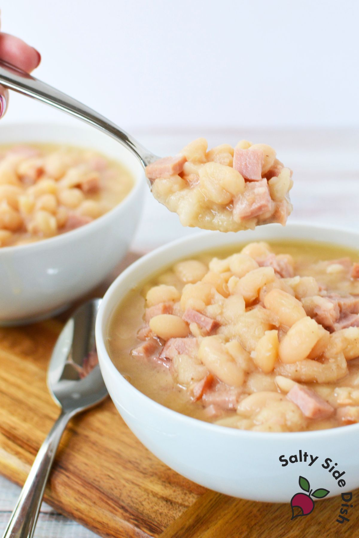 Two bowls of crockpot ham and beans served with spoons