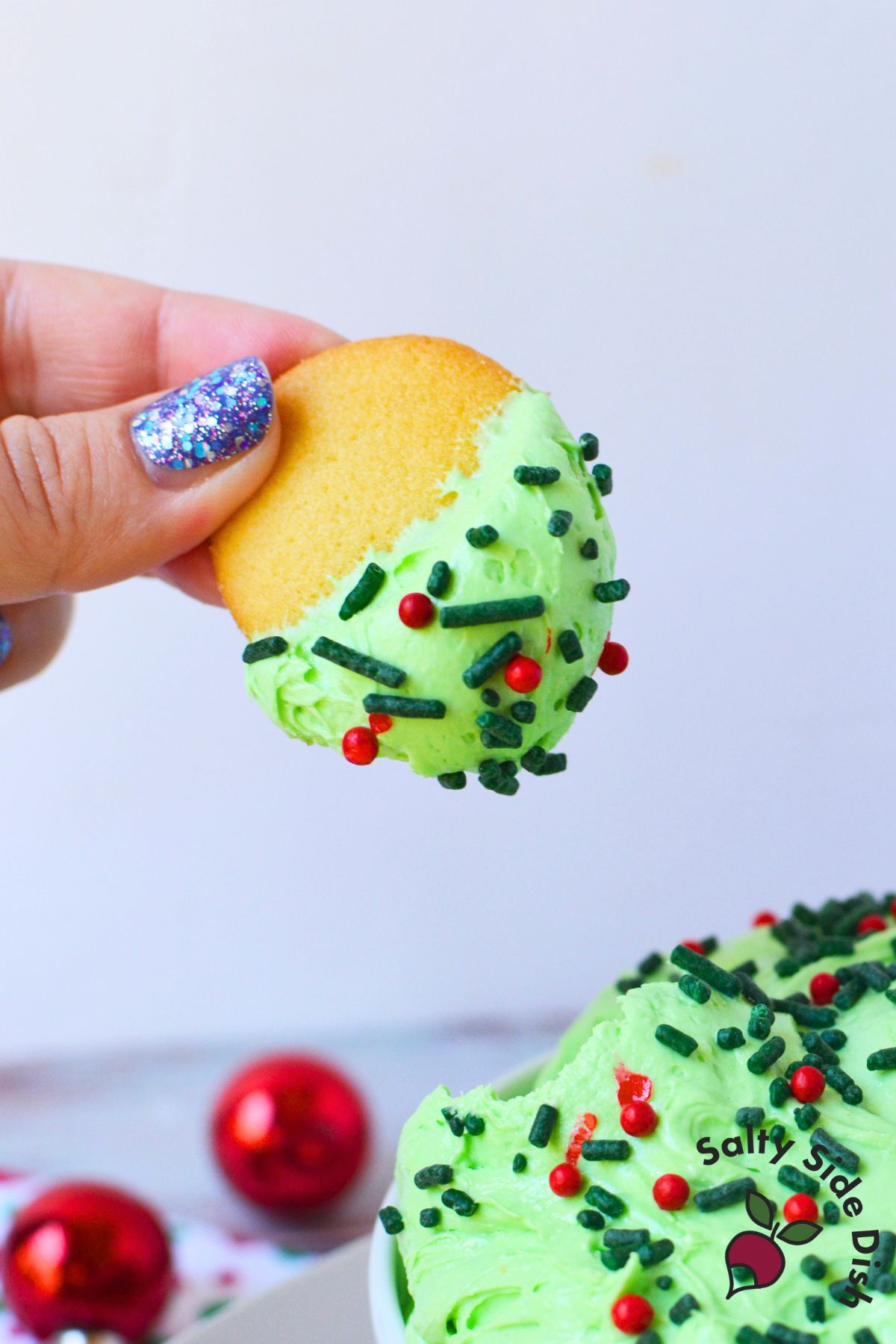 Vanilla wafer dipped into green Whoville dessert dip topped with red and green sprinkles
