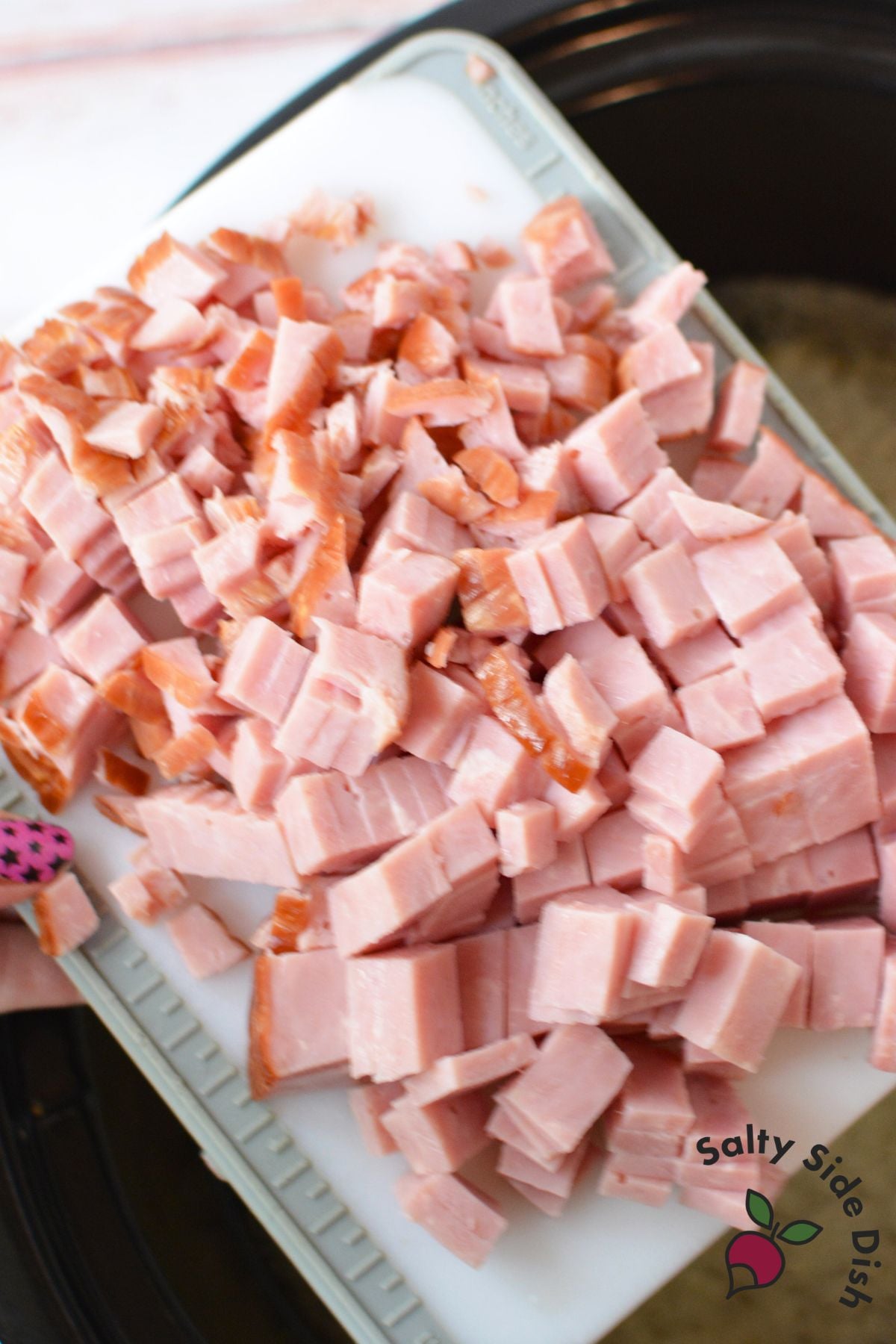 Diced ham pieces on a cutting board being added to slow cooker beans
