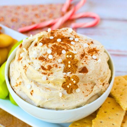 Close up of gingerbread dip topped with sprinkles and gingerbread men candies in a white serving bowl.