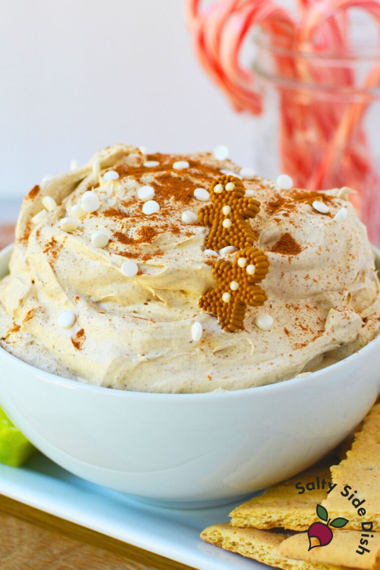 Festive gingerbread dip in a bowl decorated with sprinkles and cinnamon surrounded by crackers and apple slices.