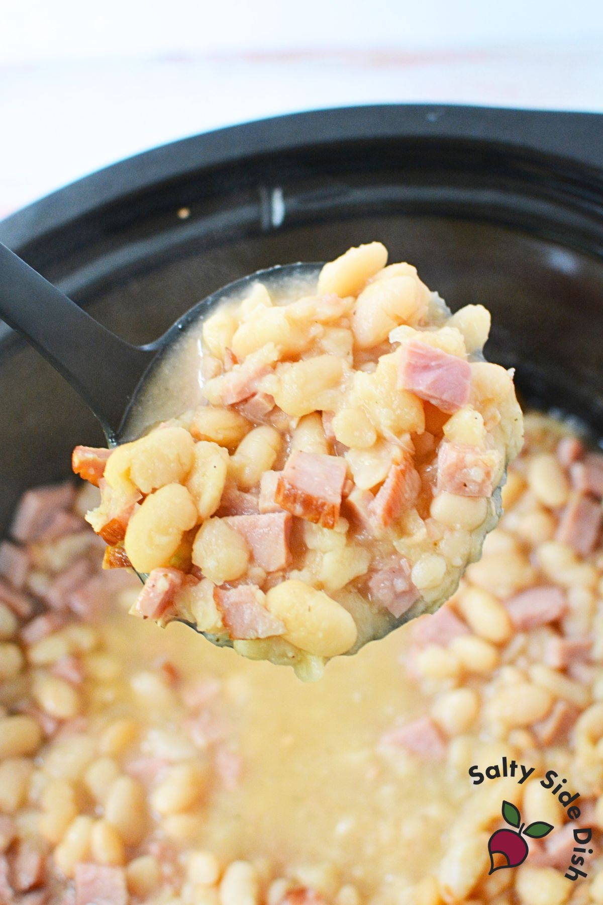Ladle scooping hearty ham and beans from a crockpot