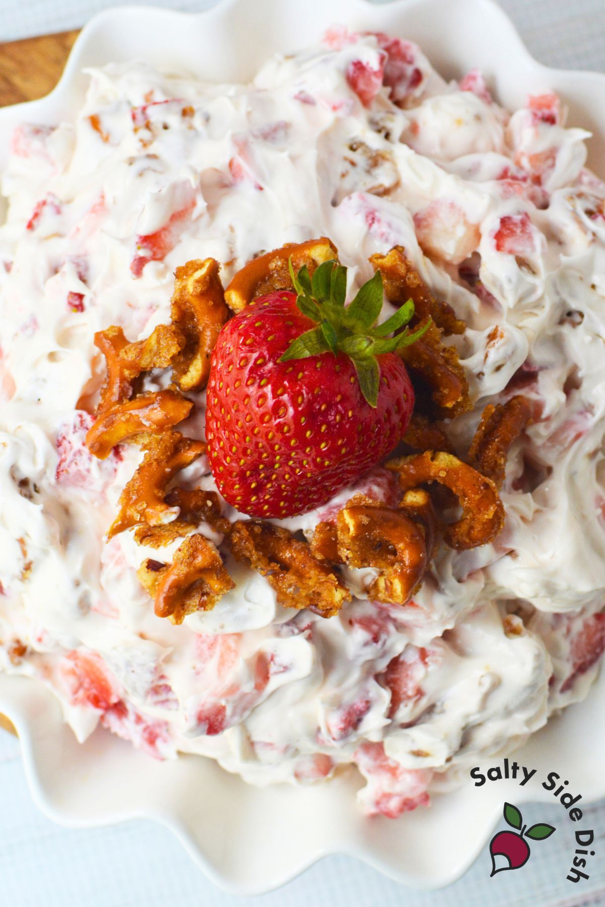 Creamy strawberry fluff salad with crushed pretzels and fresh strawberries in a white serving bowl