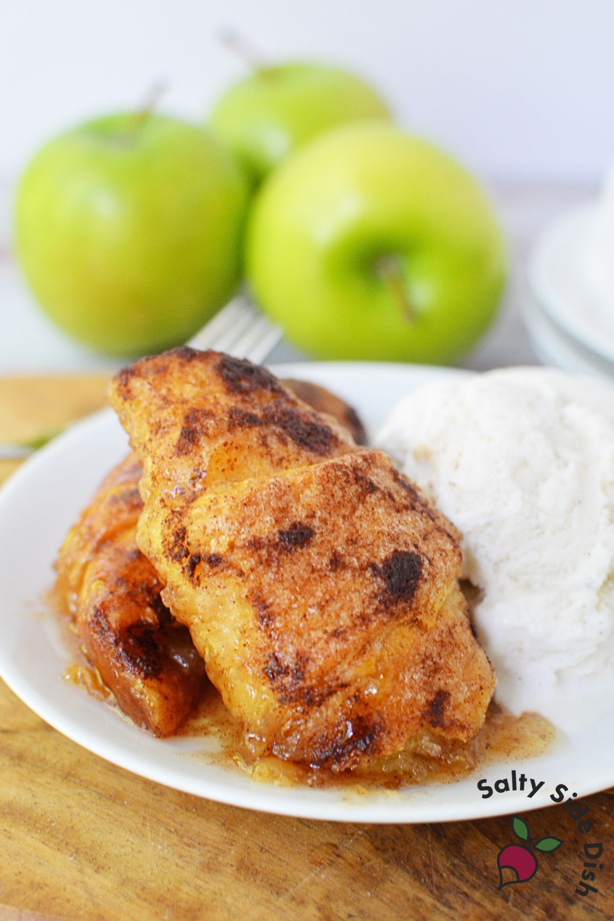 Two Mountain Dew apple dumplings on a dessert plate with a scoop of vanilla ice cream