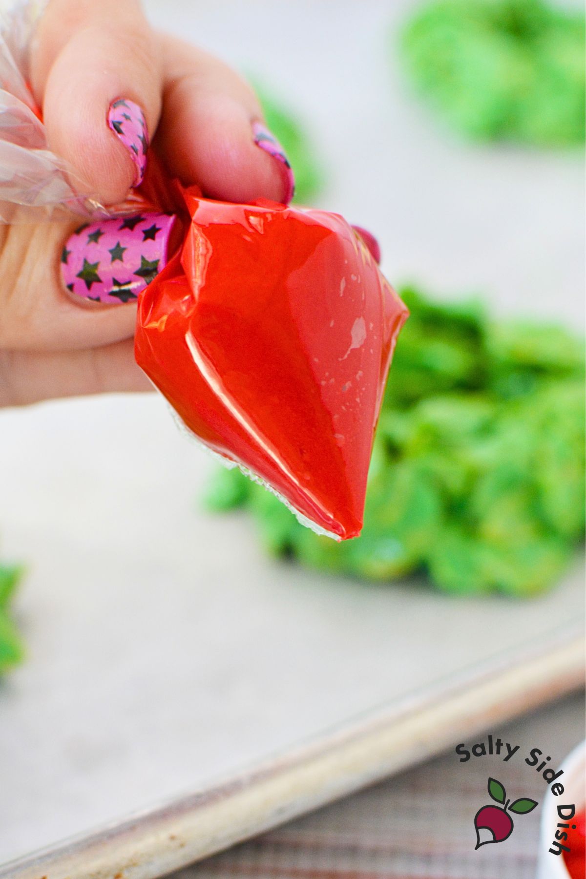 Red frosting in a piping bag used to attach cinnamon candies to cornflake Christmas wreath cookies.