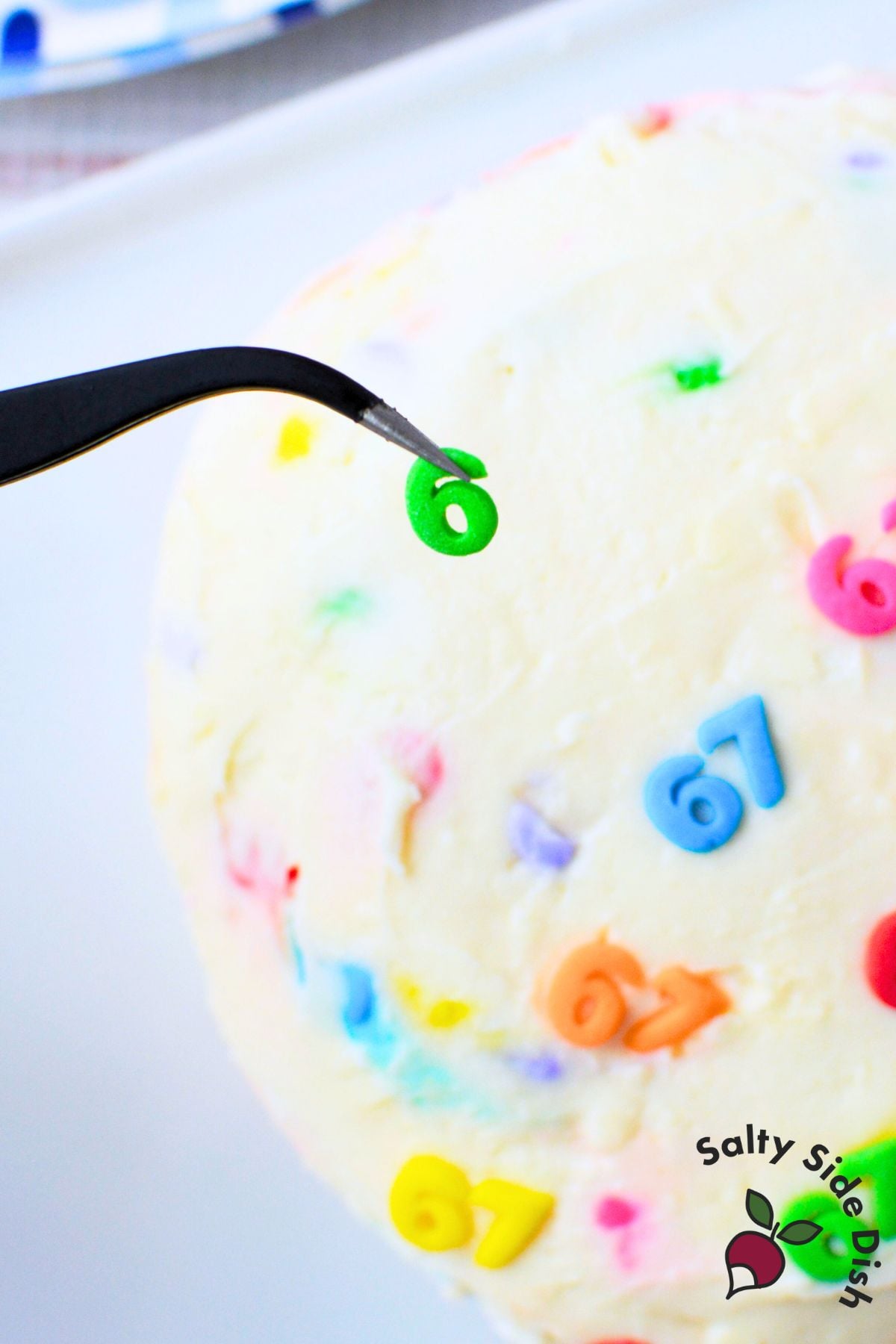 Close-up of number 6 sprinkle being placed on a sweet 6-7 cheeseball using tweezers, part of a fun kids party dessert dip.