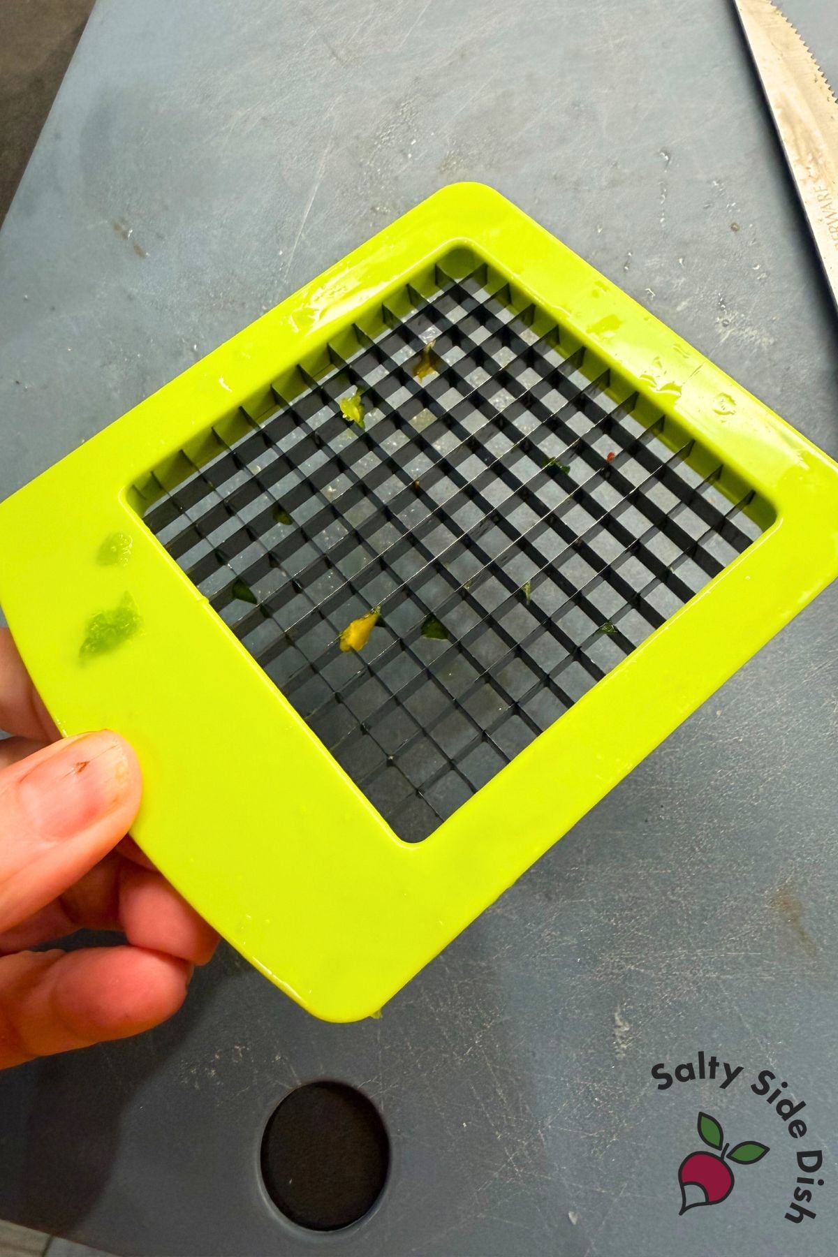 Hand holding vegetable dicer blade used to chop bell peppers into tiny pieces for rice bowl recipe