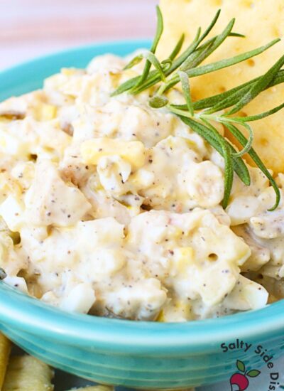 Close-up of creamy tailgate chicken salad with crackers and rosemary garnish in a turquoise bowl.