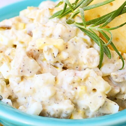 Close-up of creamy tailgate chicken salad with crackers and rosemary garnish in a turquoise bowl.