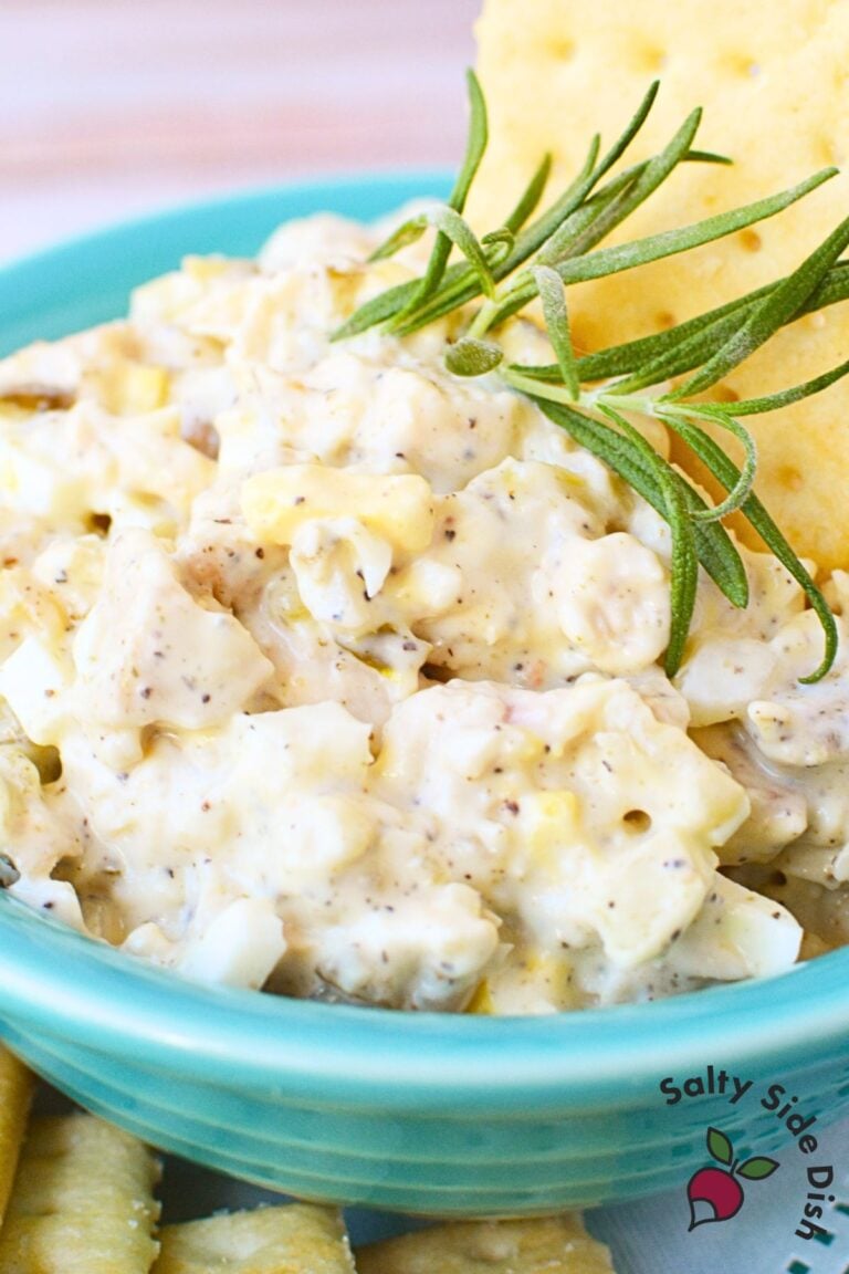 Close-up of creamy tailgate chicken salad with crackers and rosemary garnish in a turquoise bowl.